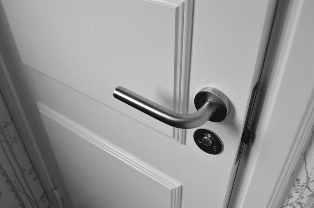 How to Clean Door Handles and High-Touch Areas Close-up of a sleek steel door handle on a white door, showcasing modern interior design in monochrome.