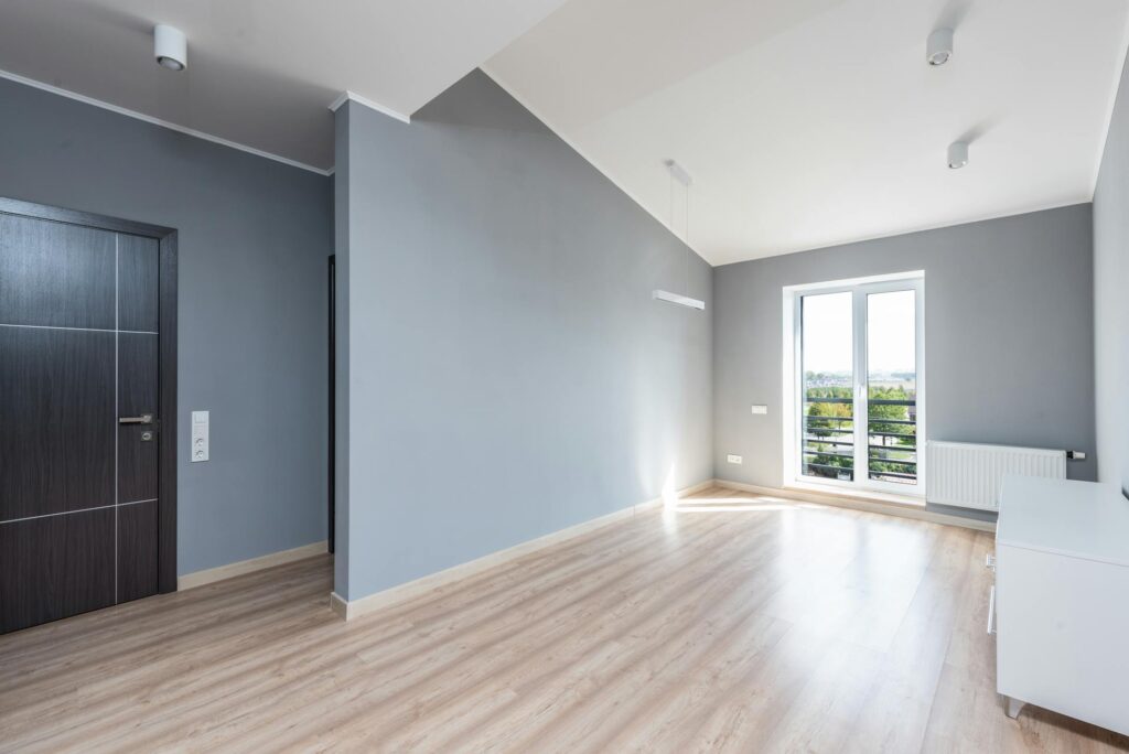 How to Clean Walls Without Ruining Paint Bright, spacious minimalist room with wooden flooring and large window view.