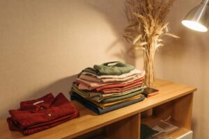 A stack of folded linen clothes on a wooden table illuminated by a warm desk lamp.