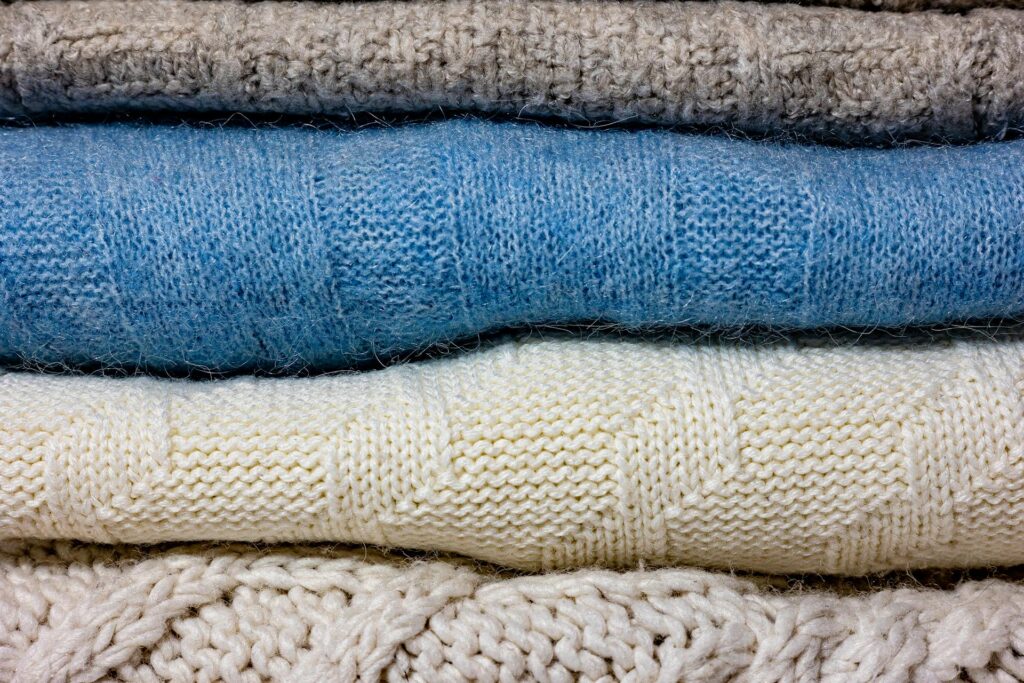 A close-up of various colorful knitted wool fabrics stacked together.