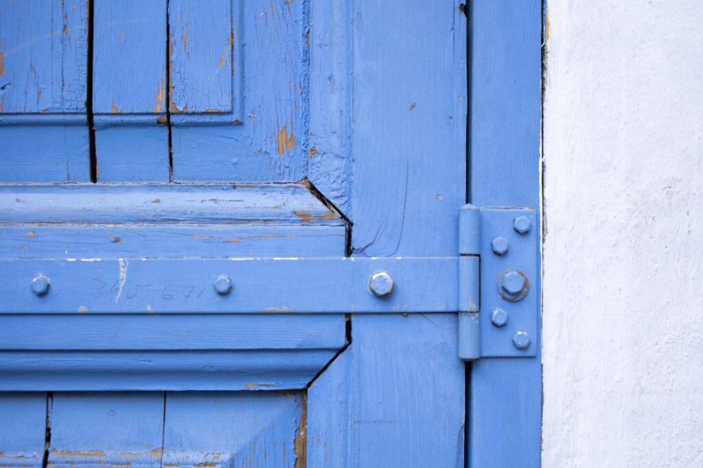 Best Lubricant for Squeaky Door Hinges Close-up of a weathered blue wooden door featuring rusty hinges and peeling paint.