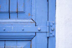 Close-up of a weathered blue wooden door featuring rusty hinges and peeling paint.