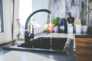 How to Fix a Dripping Faucet A modern kitchen sink with running water, a sleek faucet, and a vase on the countertop.