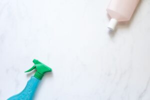 How to Clean Your Home Using Fewer Products Flat lay of cleaning spray and bottle on a white surface with ample copy space.