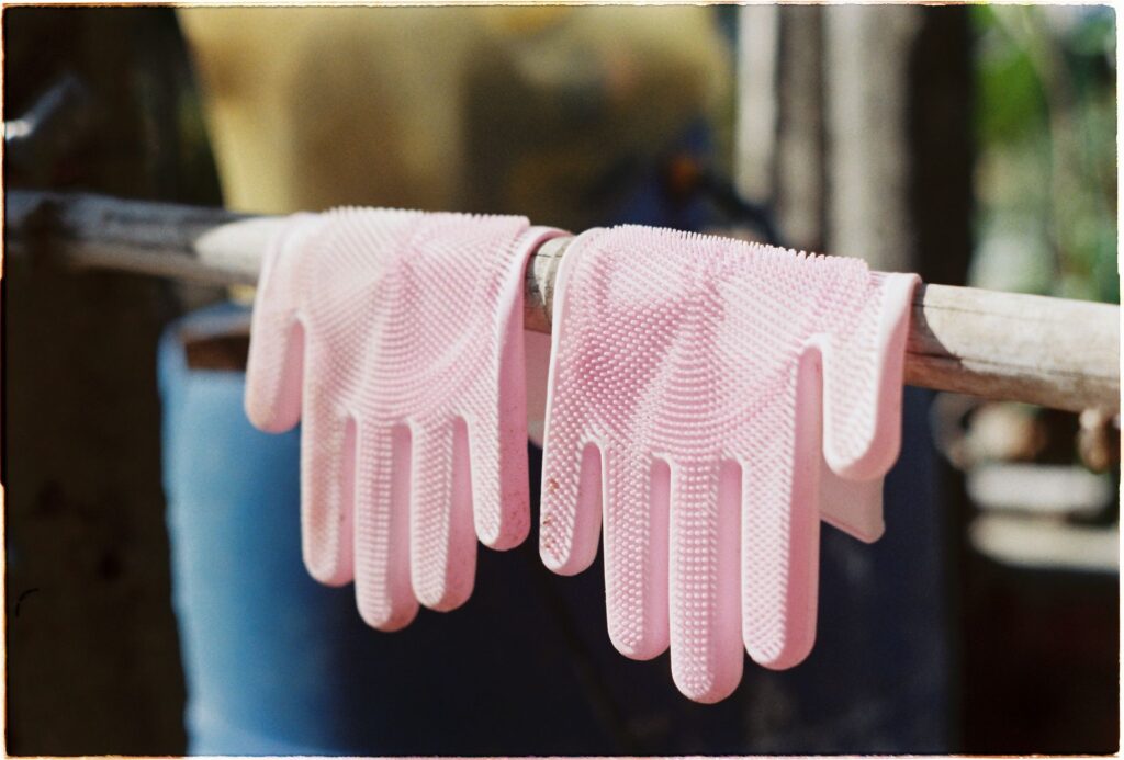 Two pink rubber cleaning gloves hanging to dry on a wooden stick outdoors in sunlight.