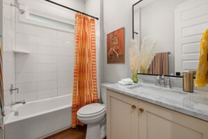 Bright bathroom featuring an orange-striped shower curtain and a marble countertop for a modern look.